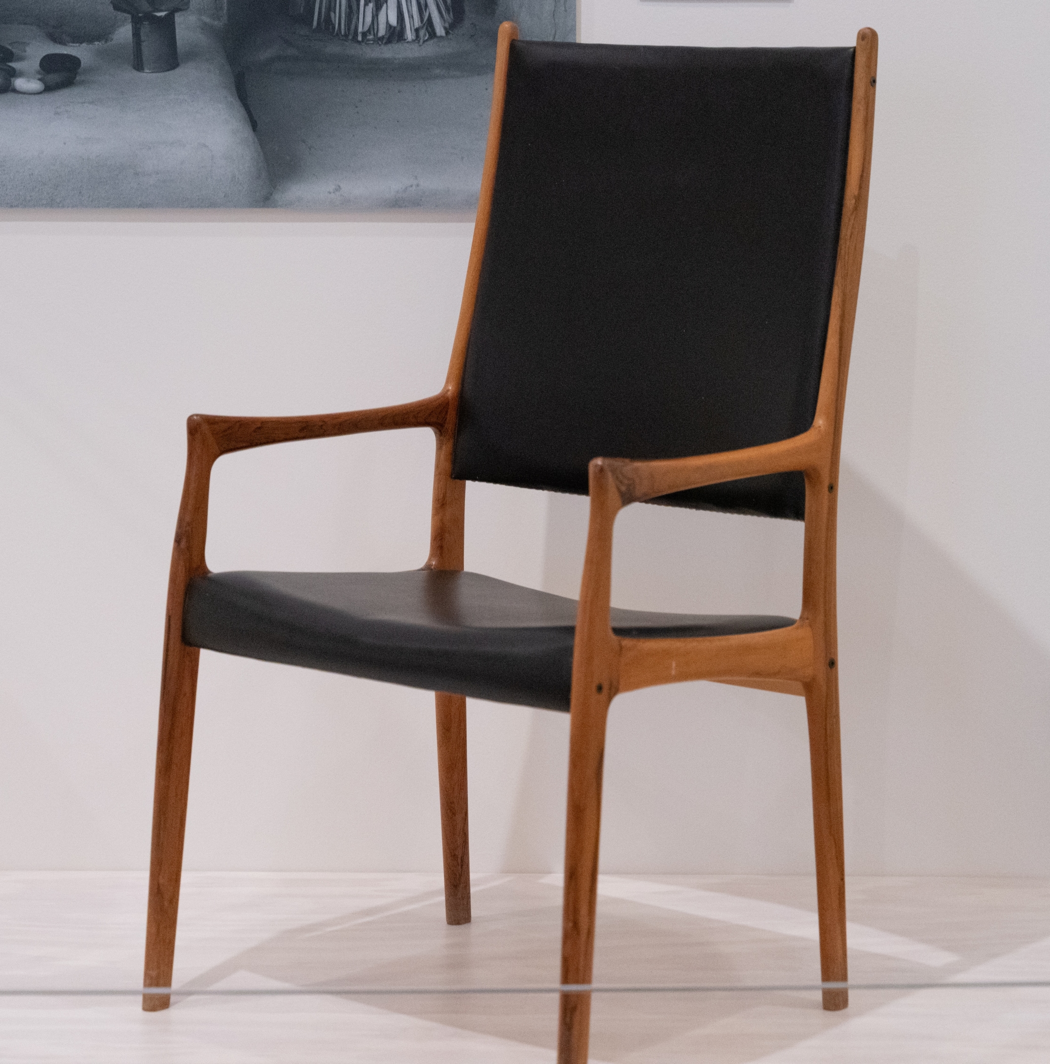 A chair with caramel colored wood shaped smoothly and organically with a black leather seat and back sits against a white background.